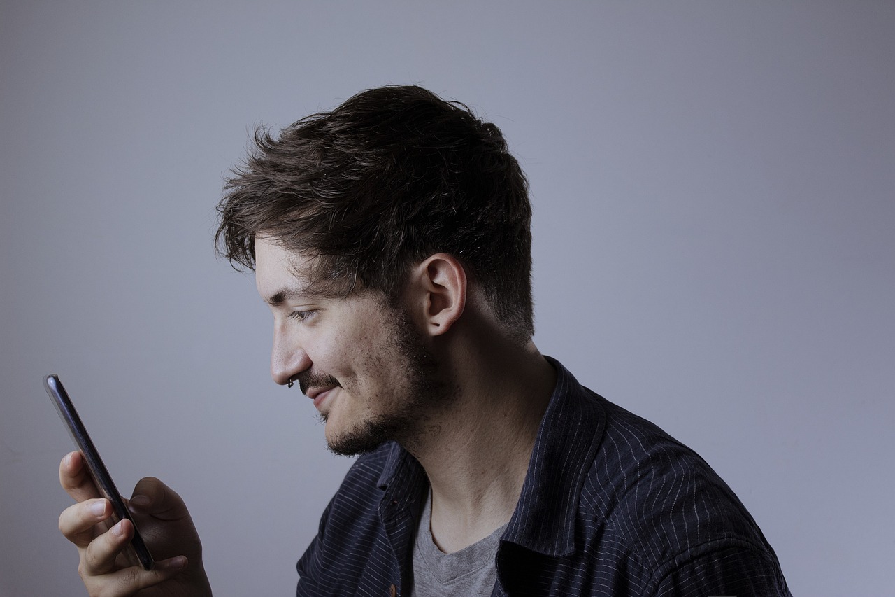 Homem branco de perfil olhando para celular.